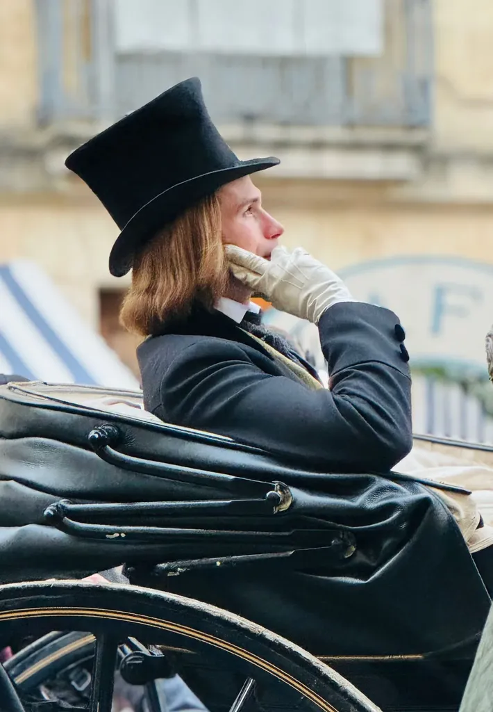 Un jeune homme aux cheveux longs, haut-de-forme et gants clairs, assis dans une calèche, la main sur le visage, en couleur.