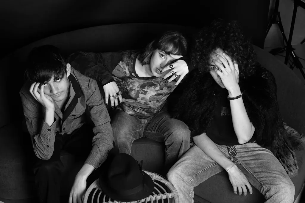 Trois jeunes gens affalés sur un canapé rond regardent l’objectif, un chapeau posé au sol, en noir et blanc.