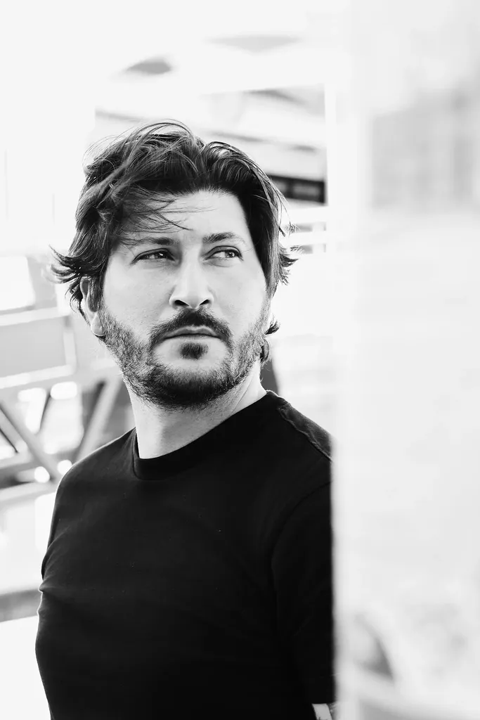 Un homme barbu en t-shirt noir regarde de côté, lumière blanche douce, en noir et blanc.