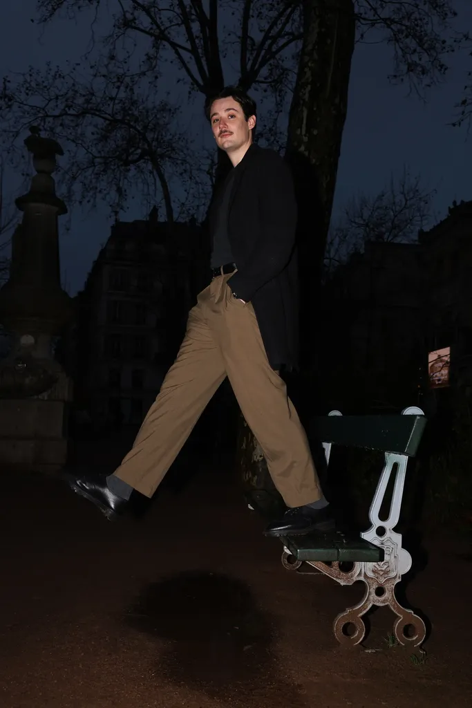 Un jeune homme en pantalon beige saute près d’un banc, de nuit, dans un jardin public.