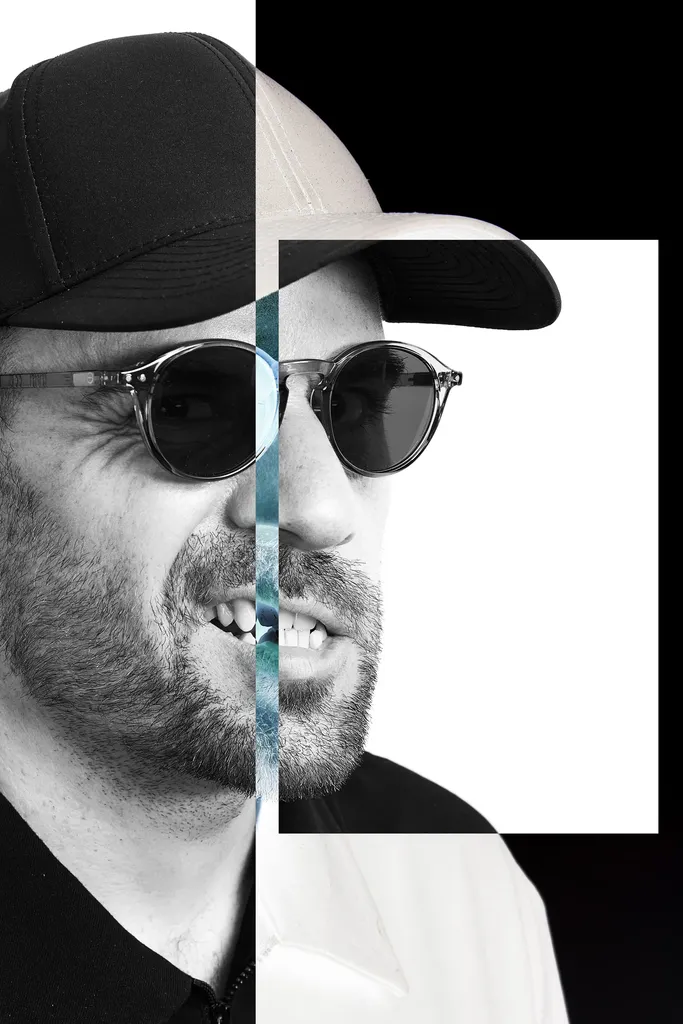Portrait en noir et blanc d’un homme barbu en casquette et lunettes de soleil, coupé verticalement en deux moitiés décalées, l’une sur fond noir, l’autre devant un rectangle blanc, avec une fine bande bleutée au centre.