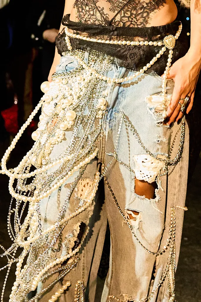Couleur, gros plan à la taille : un jean déchiré couvert de rangs de perles et de chaînes, sous un haut en dentelle noire.
