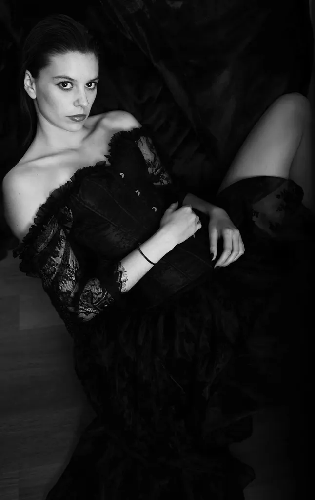Noir et blanc : une femme allongée en robe de dentelle noire épaules nues, regard vers l’objectif.