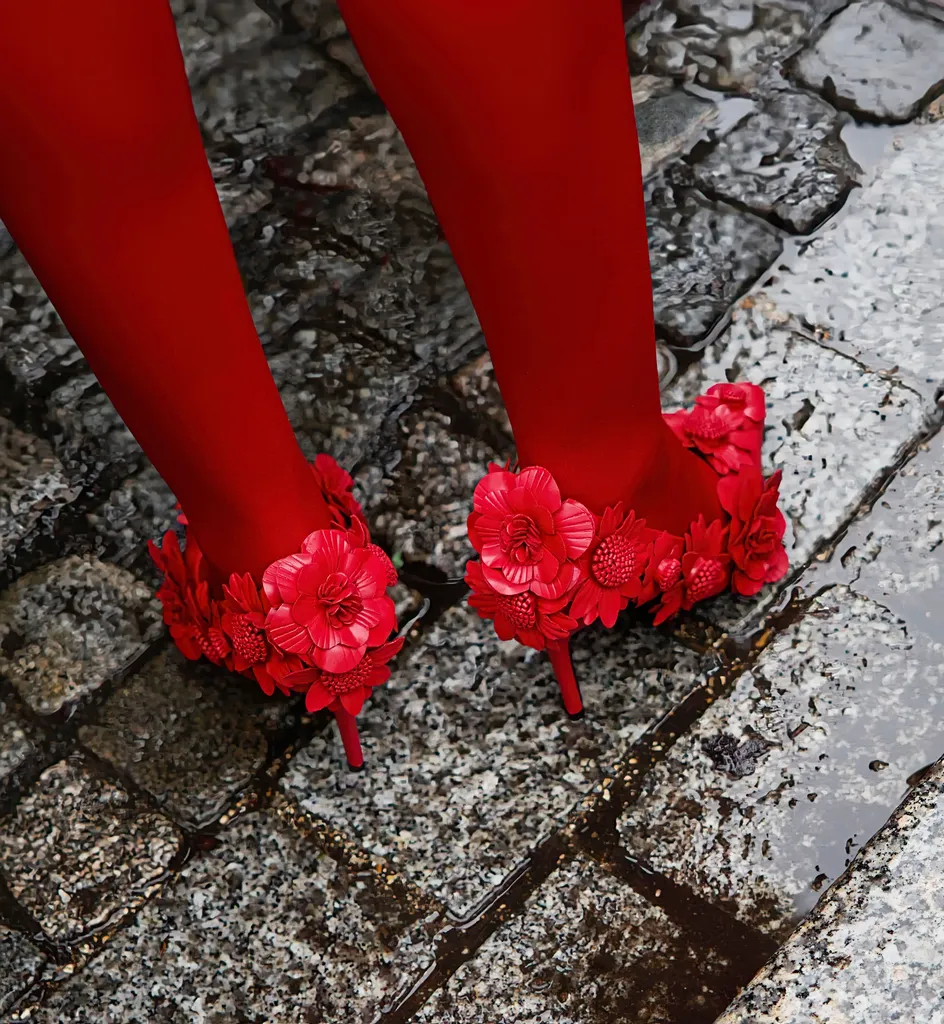 Couleur, gros plan sur des pavés mouillés : des collants rouges et des escarpins couverts de fleurs rouges.