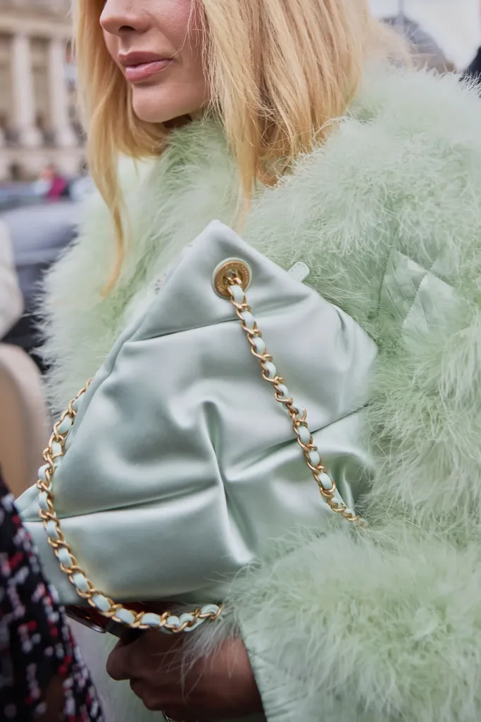 Couleur, gros plan : un sac matelassé vert d’eau à chaîne dorée tenu contre un manteau de plumes de la même couleur.