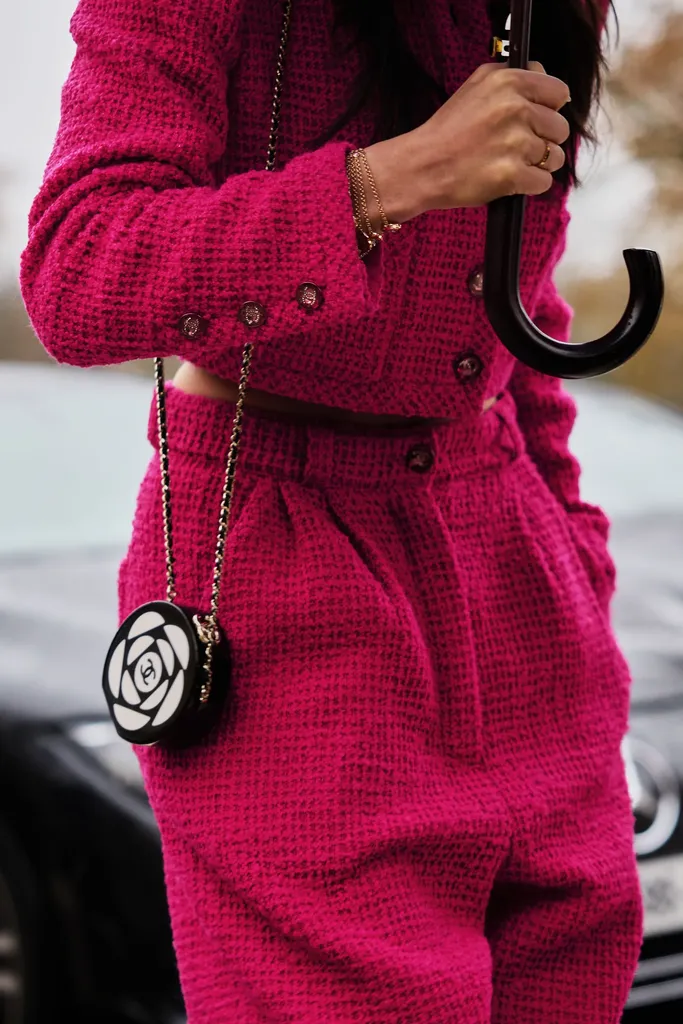 Couleur, gros plan : un tailleur en tweed fuchsia, une petite pochette ronde noire et blanche et un parapluie à poignée courbe.