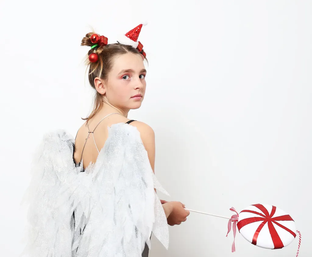 Jeune fille de dos avec des ailes blanches, une sucette rayée rouge et blanc à la main, regard par-dessus l’épaule, fond blanc.