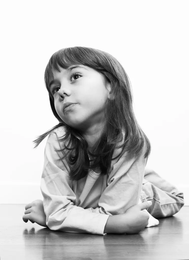 Fillette allongée sur le parquet, appuyée sur les coudes, le regard vers le haut, en noir et blanc.