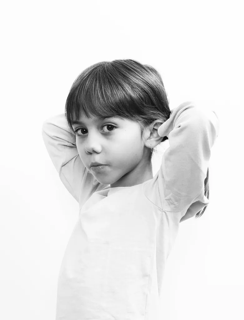 Garçon les mains derrière la tête, tee-shirt clair, sur fond blanc, en noir et blanc.