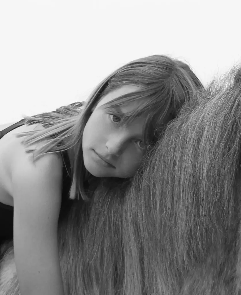 Jeune fille la joue posée contre la crinière d’un cheval, en noir et blanc.