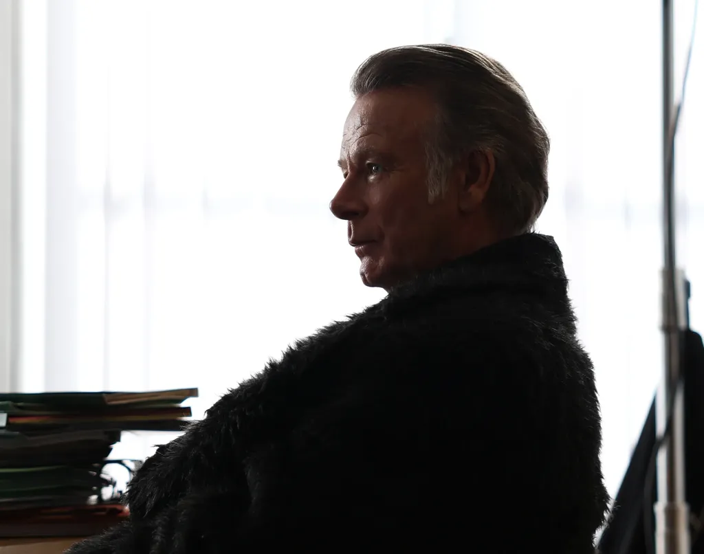 Landscape frame: a man seated in profile, silhouetted against a very bright window, files laid in front of him.