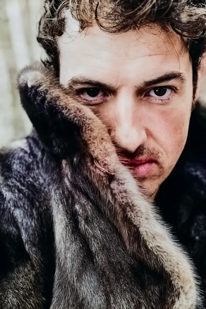 Close portrait of a man with an intense gaze, his face half hidden by a fur collar held against his cheek.