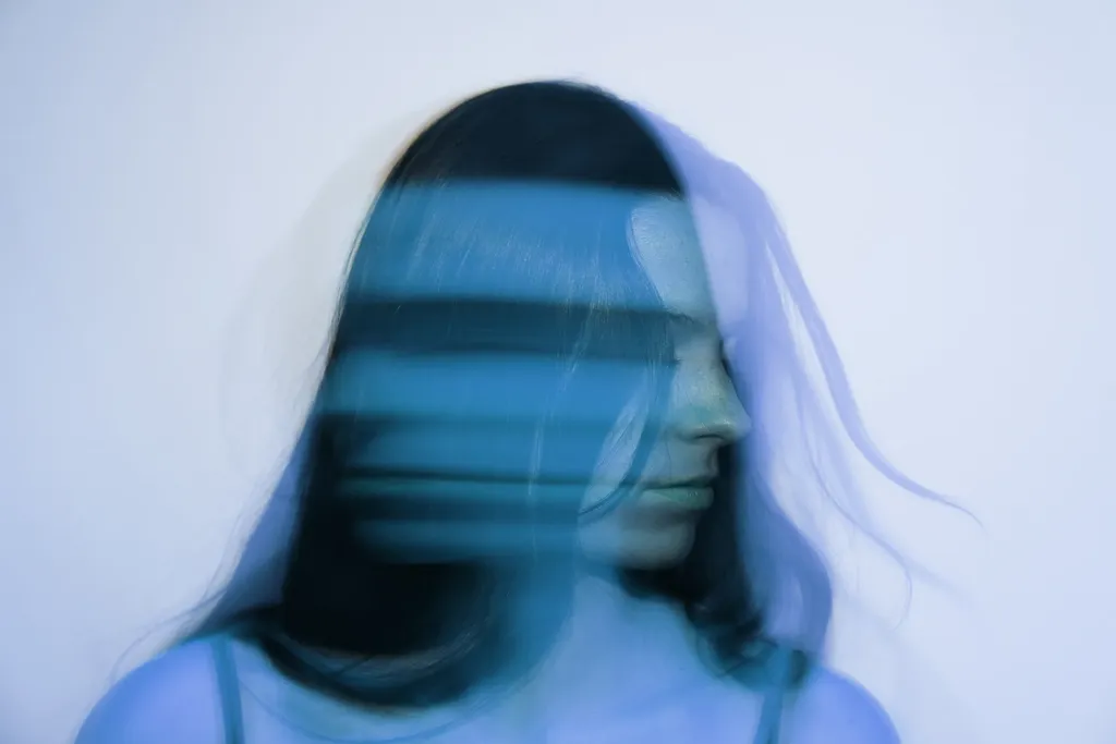 Colour landscape image: a woman with long dark hair photographed in motion, her face stretched into blurred blue bands.