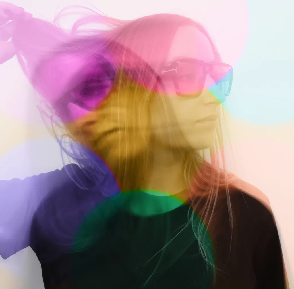 Colour multiple exposure: a woman with long hair and sunglasses, crossed by circles of pink, yellow, green and violet.